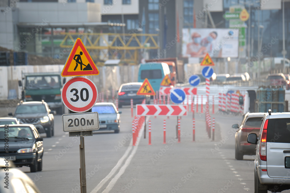 © bilanol - Roadworks warning traffic signs of construction work on city street and slowly moving cars
