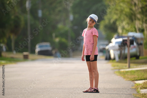 Sad moody tired young child girl standing bored alone looking in camera on park alley on sunny summer day