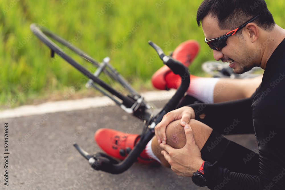 Obraz premium Bike injuries. Man cyclist fell fell off road bike while cycling. Bicycle accident, injured knee. Road in Thailand.