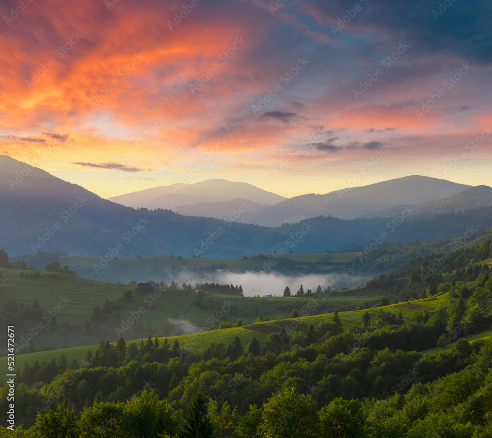 Dramatic vibrant sunset sky with clouds over the green mountain range. Foggy Carpathian mountains. Ukraine.