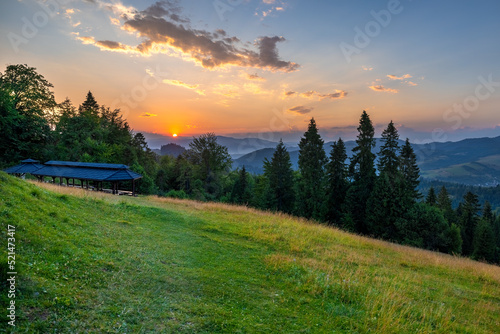 Landscape view of green meadow on the hill with mountains in the background before sunset