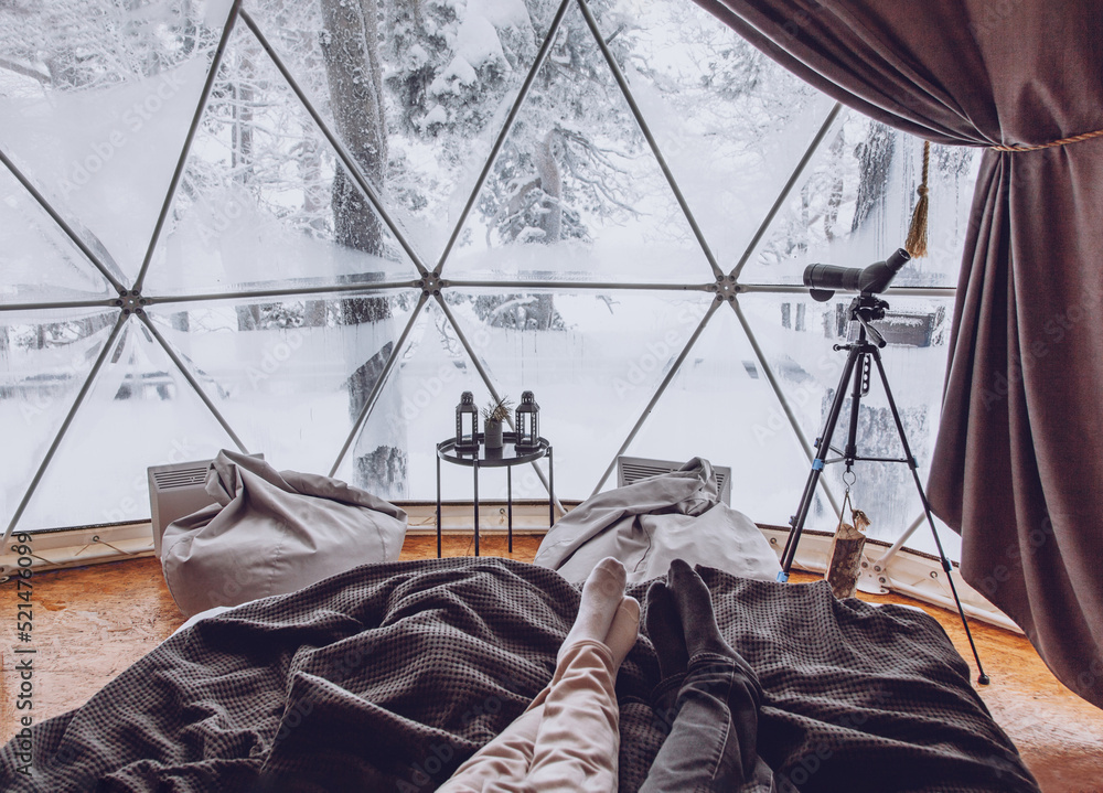 Legs of a man and woman couple in bed against the background of a snow-covered forest in a dome camping.