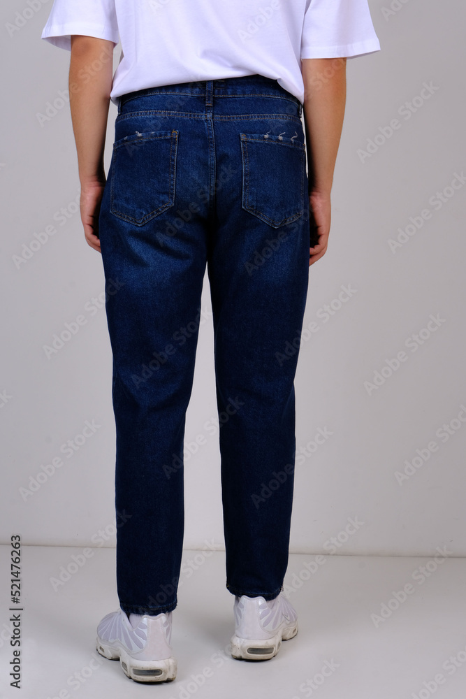 slender man in spring street clothes: skinny blue jeans and a white T-shirt. body parts: elastic male ass. concept: men's health and hemorrhoid pain. image for clothing catalog slender man in spring street clothes: skinny blue jeans and a white T-shirt. body parts: elastic male ass. concept: men's health and hemorrhoid pain. image for clothing catalog
