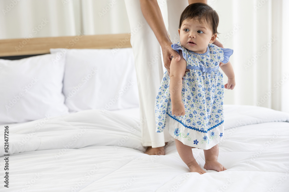 baby girl learning to walk and mother or sitter support her on bedroom baby girl learning to walk and mother or sitter support her on bedroom