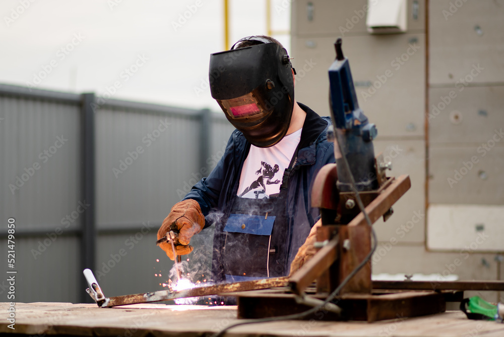 The man works with a welding machine. He is wearing a welder's protective mask and protective gloves. A rare working profession. The man works with a welding machine. He is wearing a welder's protective mask and protective gloves. A rare working profession.