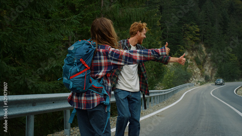 Two backpackers hitchhiking road. Couple tourists catch wait car in mountains.