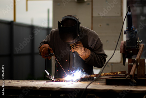 The man works with a welding machine. He is wearing a welder's protective mask and protective gloves. A rare working profession.