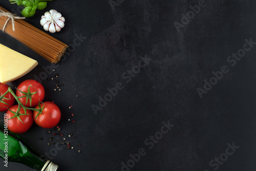 Spaghetti, tomatoes, garlic, basil, pepper, cheese, olive oil on a dark background with space for writing text.