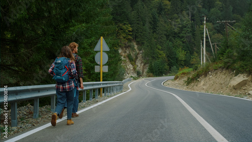 Couple hitchhikers walk mountains. Two travelers trekking on roadside highway. © stockbusters