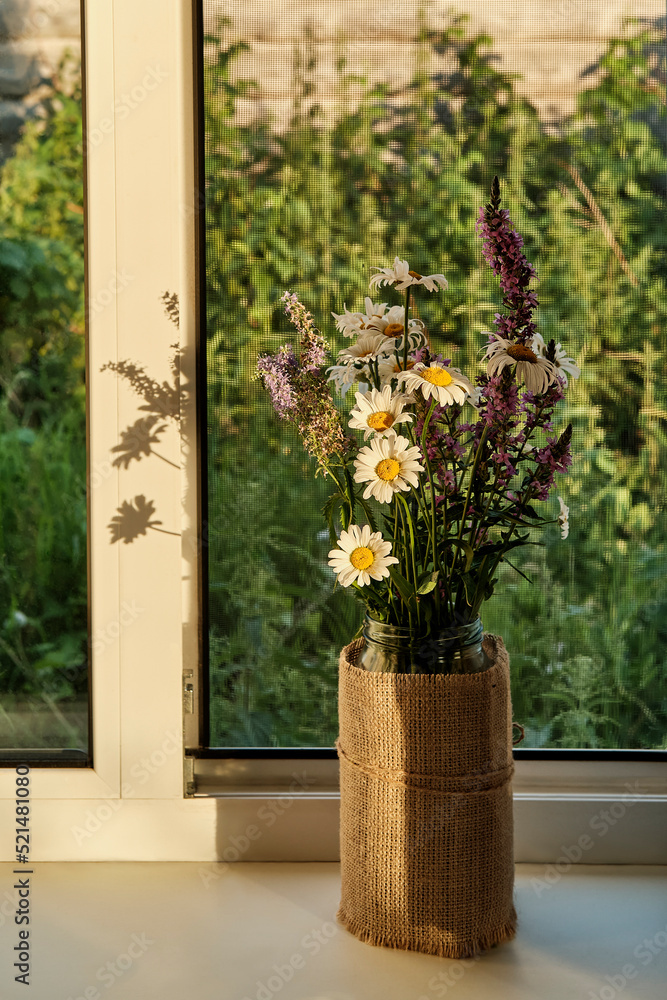 Bouquet of wild meadow flowers on window sill of rural house in sunset sunlight.