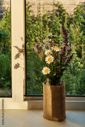 Bouquet of wild meadow flowers on window sill of rural house in sunset sunlight. © IrinaK