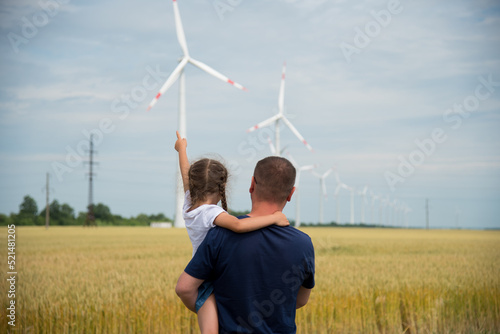 A girl and her dad look at the wind generator in the field. Ecology. Future.