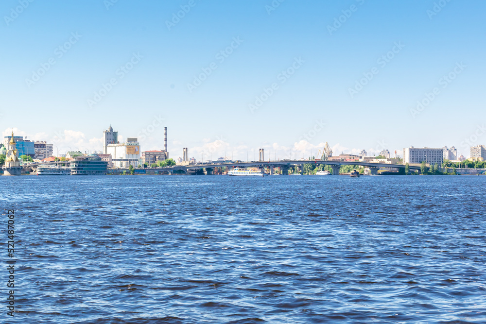 Scenic nature travel cityscape river Dnipro with blue water and metal pedestrian bridge at sunny summer day in Kiev. View from inside river, ship on water-Kiev Ukraine,11 June 2021
