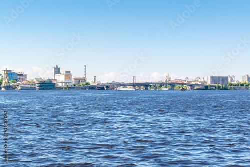 Scenic nature travel cityscape river Dnipro with blue water and metal pedestrian bridge at sunny summer day in Kiev. View from inside river, ship on water-Kiev Ukraine,11 June 2021 © Дарья Воронцова