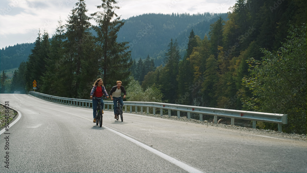 Millennials riding bikes together in mountains landscape. Hipsters cycling road.