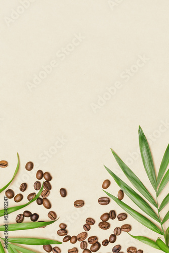Coffee background suitable for caffeine and coffee producers. Natural coffee beans and palm leaves on a craft paper with copy space. Harvest coffee. Vertical orientation