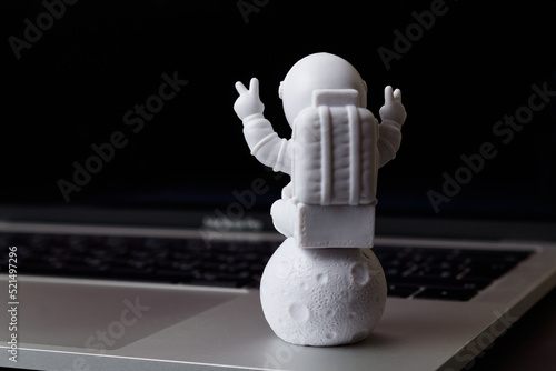 A toy astronaut sits on the moon on a laptop. The astronaut sits on the moon. Application of technology in space. Space technologies. Cosmonautics Day. Back view. Close-up. Copy space