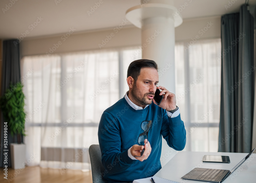 Stressed entrepreneur discussing on smart phone while working on laptop at desk. Stressed entrepreneur discussing on smart phone while working on laptop at desk.