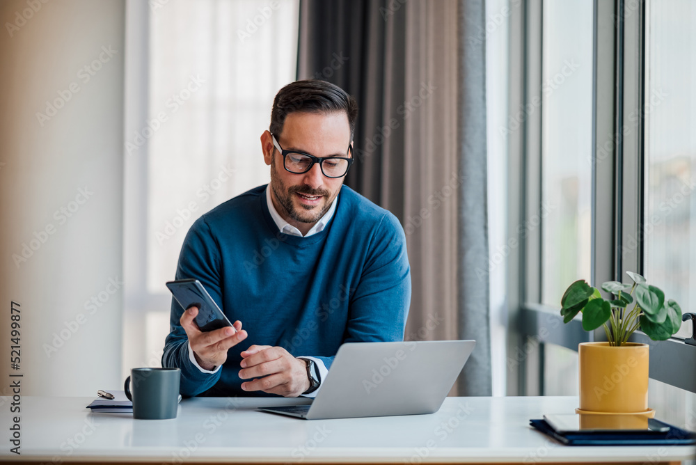 Professional messaging on smart phone while working on laptop at office desk. Professional messaging on smart phone while working on laptop at office desk.
