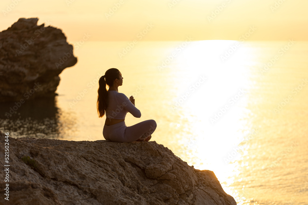 silhouette of young woman practice yoga and meditation near the sea at sunrise, healthy lifestyle concept, lotus position