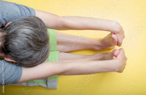 A middle-aged woman is doing yoga on a mat, bent over with her hands clasping her feet. Stretching at home. Selective focus, blur.