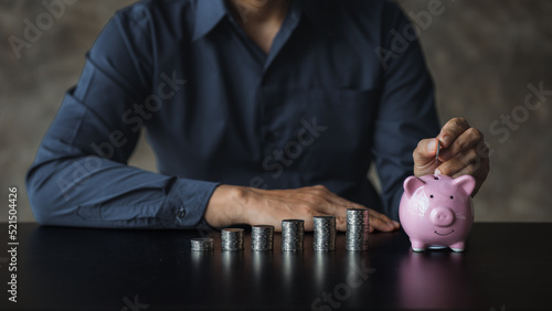 A businessman holding a coin in a piggy bank. Placing coins in a row from low to high is comparable to saving money to grow more. The concept of growing savings and saving by investing in stock funds.