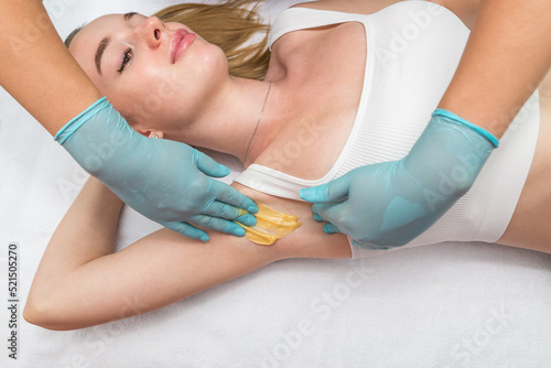 Depilation and epilation of the female armpit with liquid sugar paste. The beautician s hand applies wax paste to the armpit.