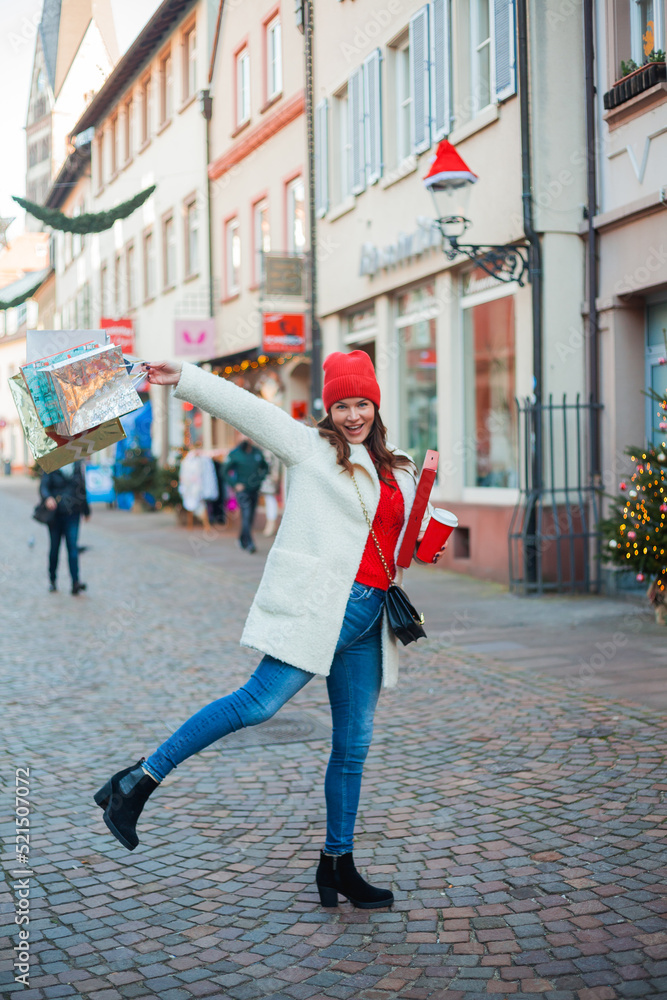 Happy young blue-eyed woman doing Christmas shopping in the center of a European city. A beautiful dark-haired model buys gifts for the winter holidays. Vacation.