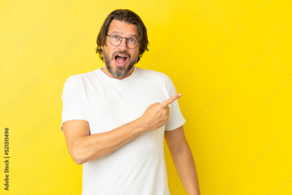 Senior dutch man isolated on yellow background surprised and pointing side Senior dutch man isolated on yellow background surprised and pointing side