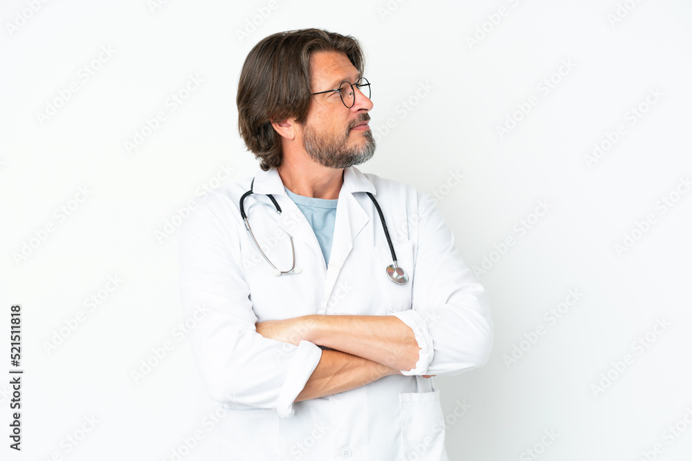 Senior dutch man isolated on white background wearing a doctor gown and with arms crossed looking side