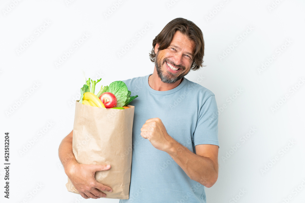 Senior dutch man holding grocery shopping bag over isolated background celebrating a victory Senior dutch man holding grocery shopping bag over isolated background celebrating a victory