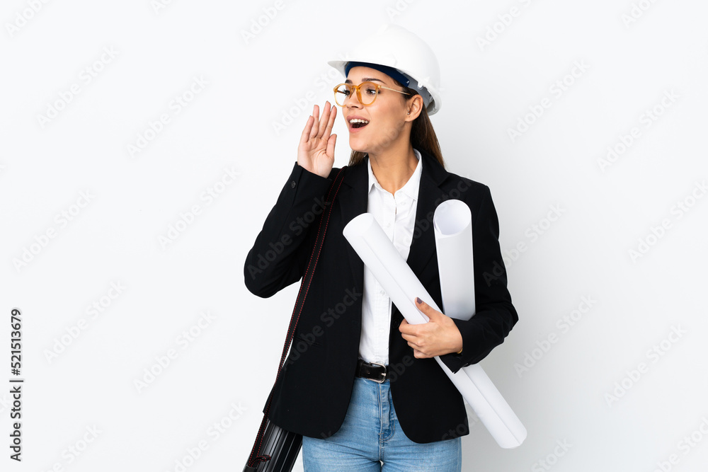 Young architect caucasian woman with helmet and holding blueprints over isolated background shouting with mouth wide open Young architect caucasian woman with helmet and holding blueprints over isolated background shouting with mouth wide open