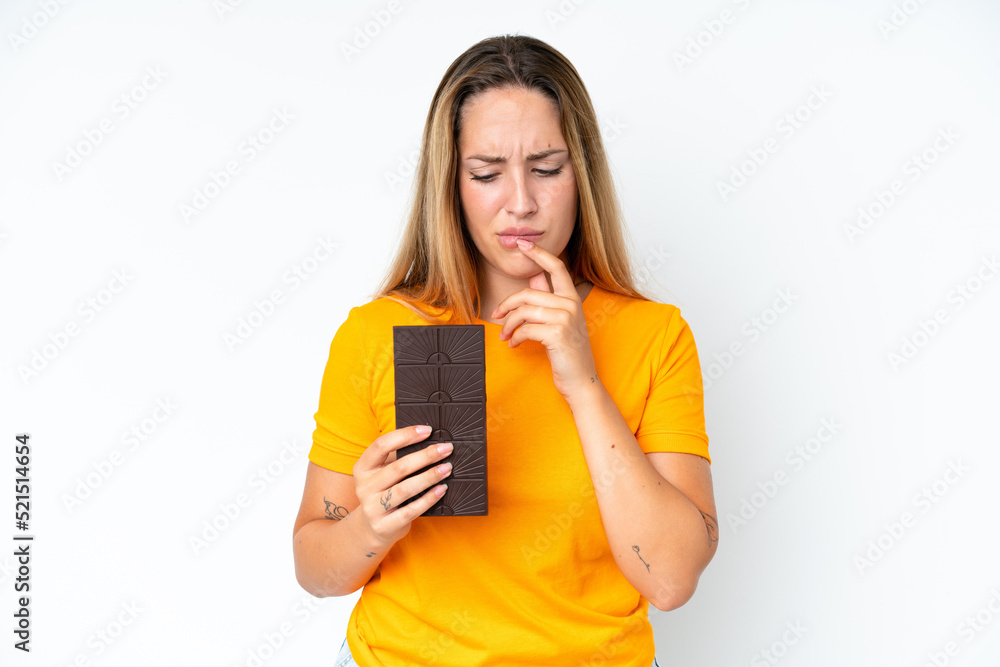 Young caucasian woman isolated on white background taking a chocolate tablet and having doubts Young caucasian woman isolated on white background taking a chocolate tablet and having doubts