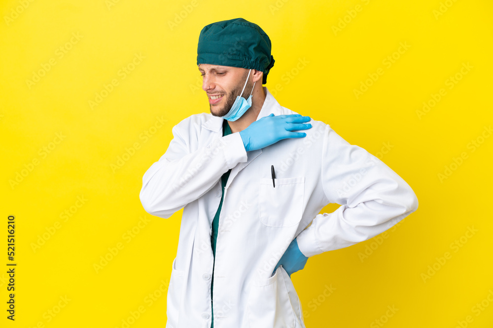 Surgeon blonde man in green uniform isolated on yellow background suffering from pain in shoulder for having made an effort Surgeon blonde man in green uniform isolated on yellow background suffering from pain in shoulder for having made an effort