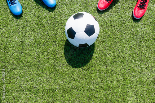 Soccer football background. Soccer ball and two pair of football sports shoes on artificial turf soccer field with shadow from football goal net on sunny day outdoors. Top view