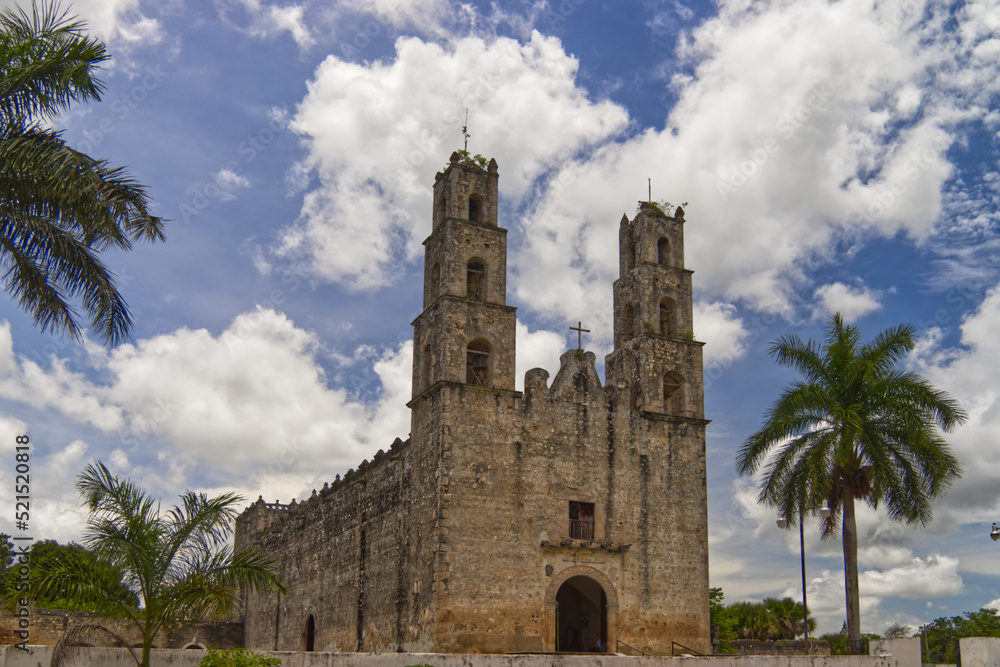 Typical church of Mexico Yucatan, blue cloudy sky and palms