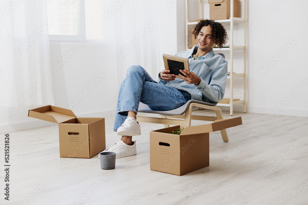 guy with curly hair sitting on a chair unpacking with box in hand moving sorting things out guy with curly hair sitting on a chair unpacking with box in hand moving sorting things out