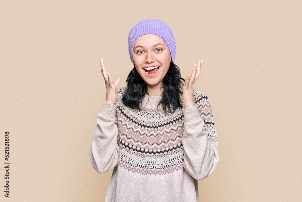 Happy emotional teenage female in sweater hat on light brown background Happy emotional teenage female in sweater hat on light brown background
