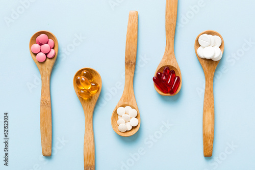 Vitamin capsules in a spoon on a colored background. Pills served as a healthy meal. Red soft gel vitamin supplement capsules on spoon