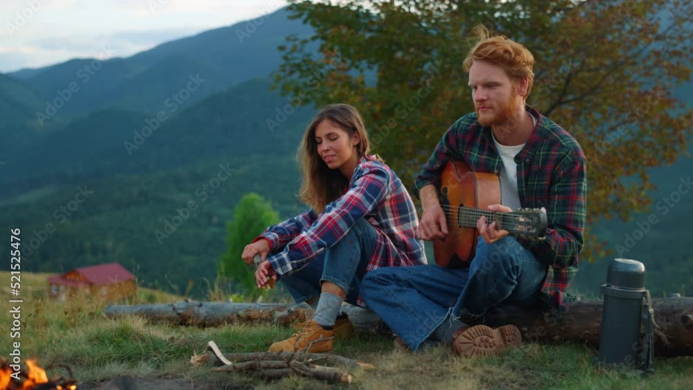 Positive couple date outdoors in mountains. Two lovers play guitar by campfire. Positive couple date outdoors in mountains. Two lovers play guitar by campfire.