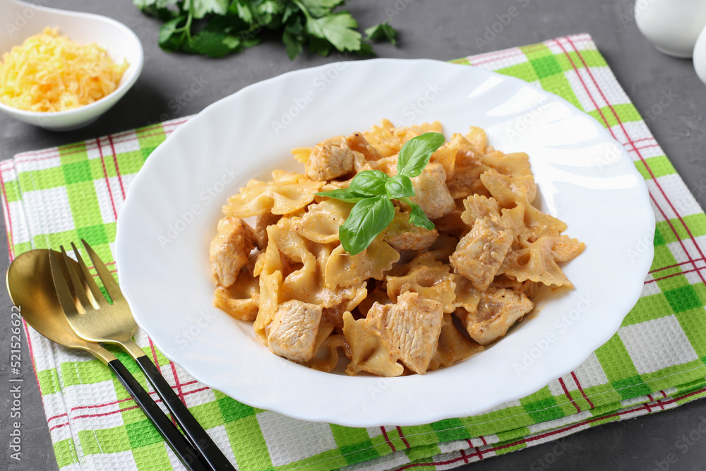 Pasta farfalle with turkey in tomato-sour cream sauce, served cheese and basil on gray background Pasta farfalle with turkey in tomato-sour cream sauce, served cheese and basil on gray background