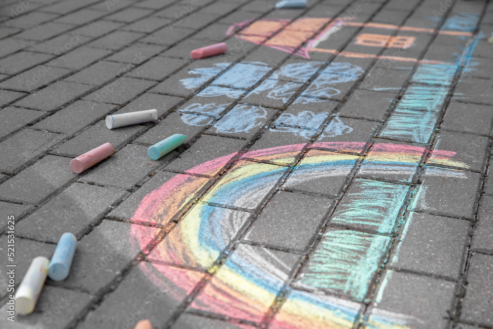 Rainbow with grass, house and clouds painted in colored chalk on a path on the street