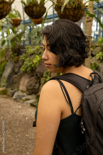 female traveler using a suitcase walking on a garden path surrounded by nature  young latin woman with short hair showing her face in profile  tourist