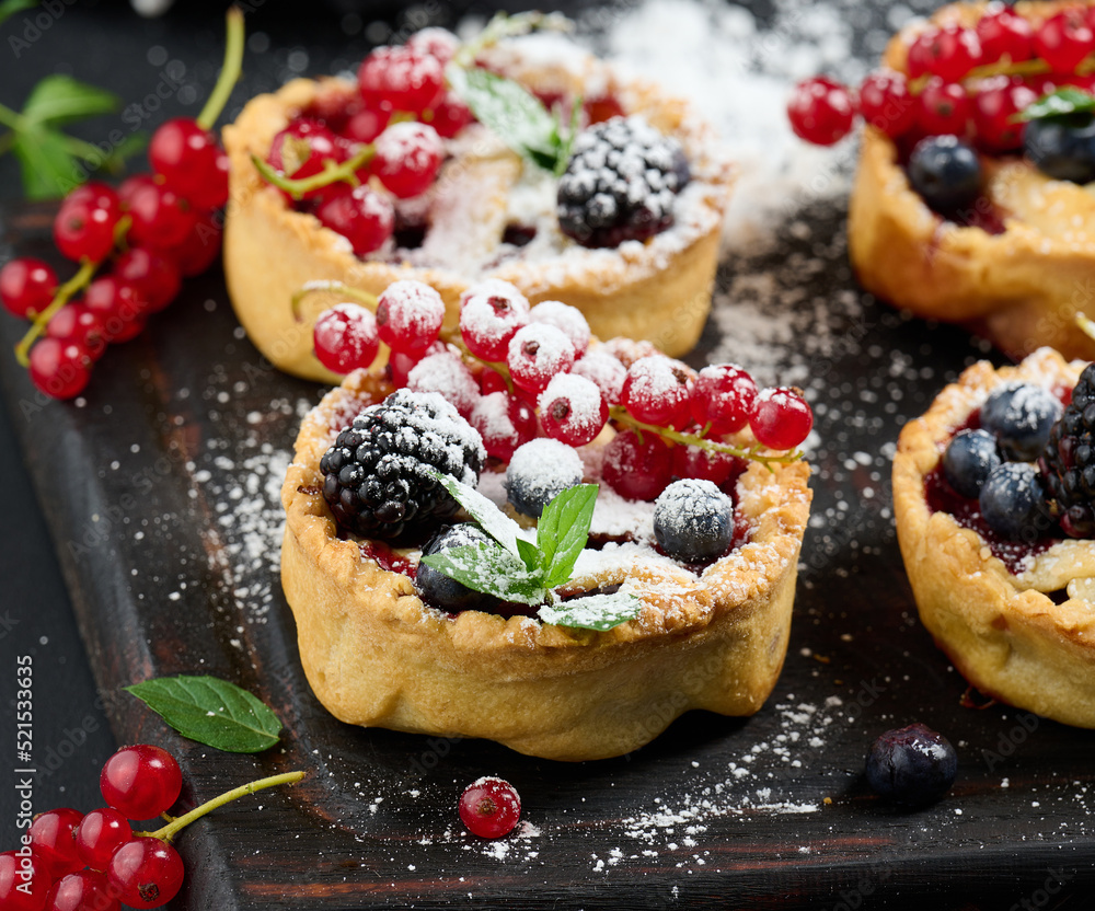 Fruit tart with red currants sprinkled with powdered sugar on a black table - obrazy, fototapety, plakaty 