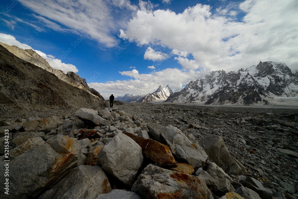 A trekker walking on the brink of Biafo glacier in the Karakoram National Park on a beautiful sunny and partly cloudy day. 