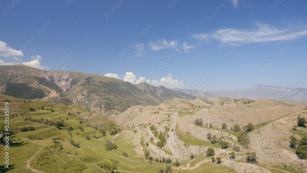 Aerial view of amazing landscape with beautiful valley on a sunny day. Action. Flying above summer mountains on blue cloudy sky background.
