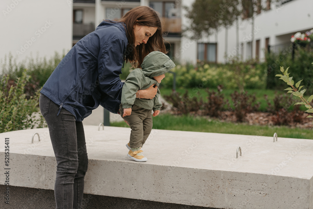 A mom is teaching her female toddler how to do steps in the street at noon.