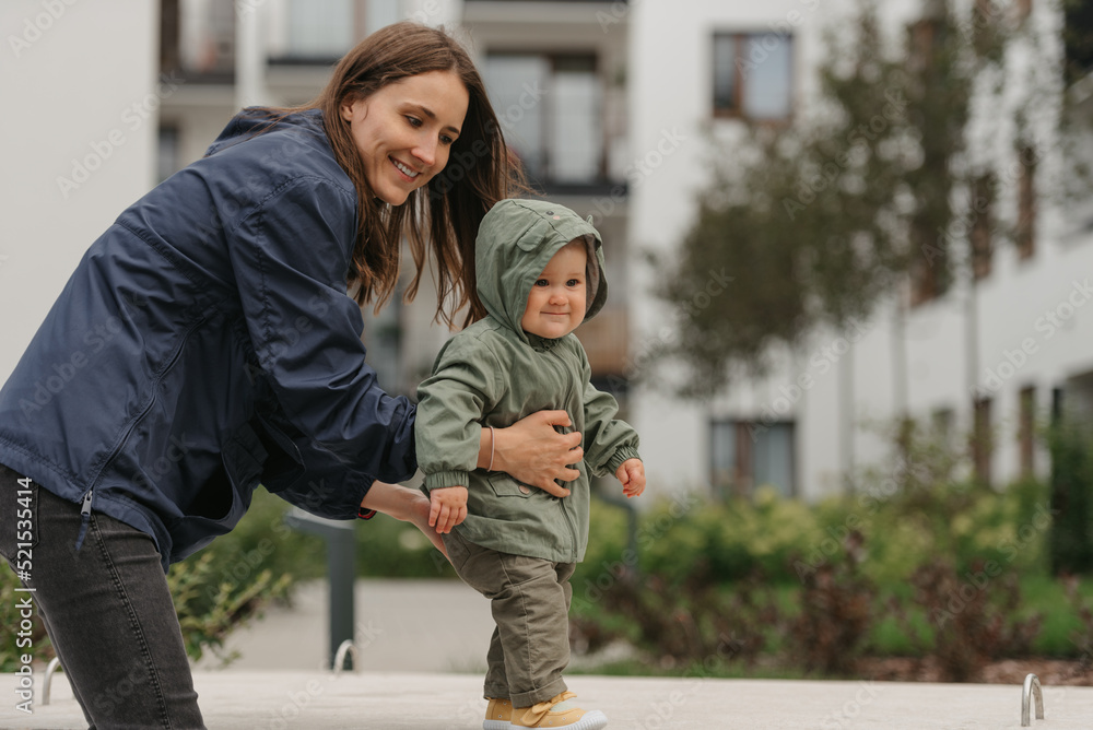 A mom is teaching her female toddler how to do steps in the street at noon.