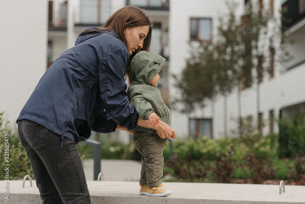 A mom is teaching her female toddler how to do steps in the street at noon.
