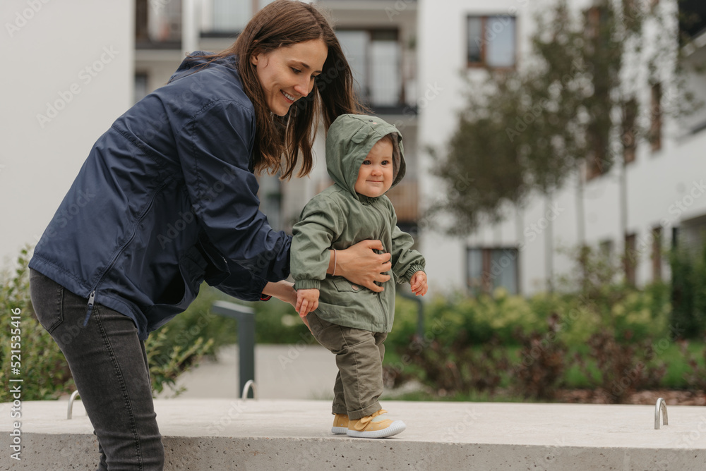 Fototapeta premium A mom is teaching her female toddler how to do steps in the street at noon.